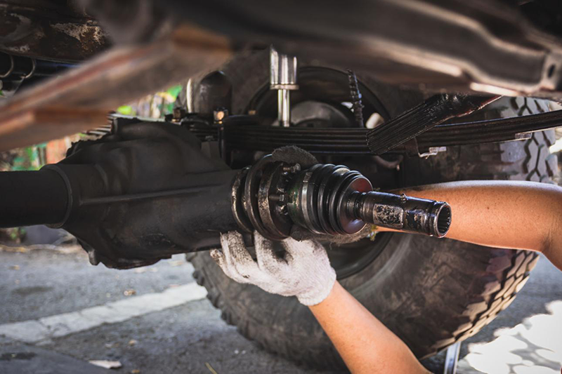 Mechanic repairing heavy-duty truck driveline component, fixing a bent driveshaft axle on an off-road Amarok after impact damage.