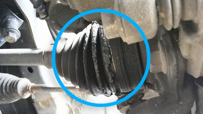 Damaged CV boot on car axle with torn rubber and leaking grease, close-up view