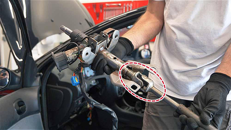 Mechanic holding a steering shaft assembly with the steering U-joint highlighted